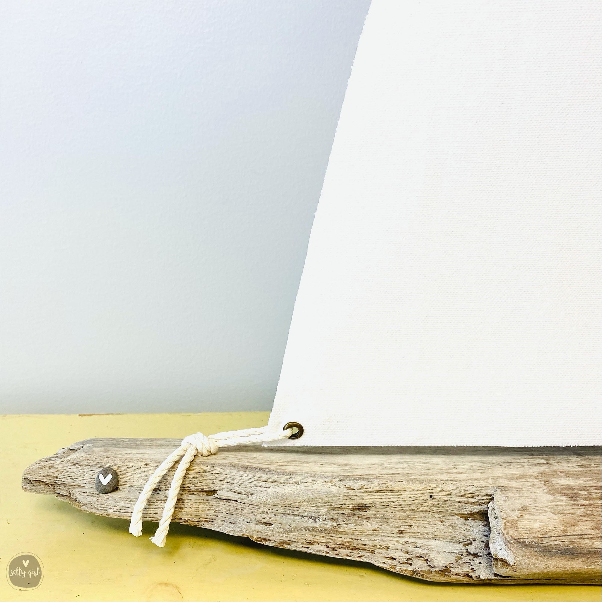 A wooden sailboat made from driftwood, with a white sail and a small heart-shaped ornament attached to the front.