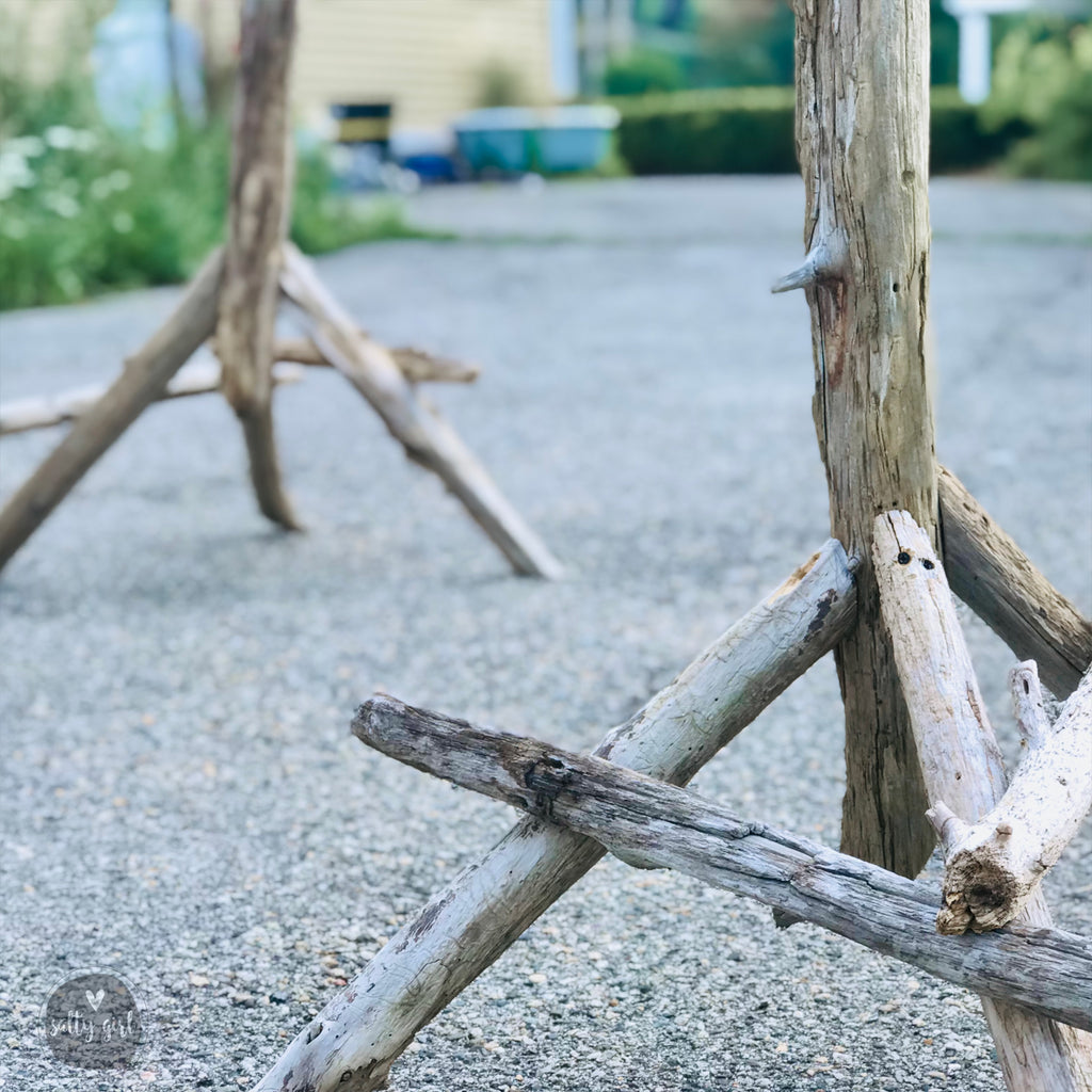 a close-up view of several wooden logs and branches arranged in a way that they appear to be connected or leaning against each other, possibly on a gravel surface.