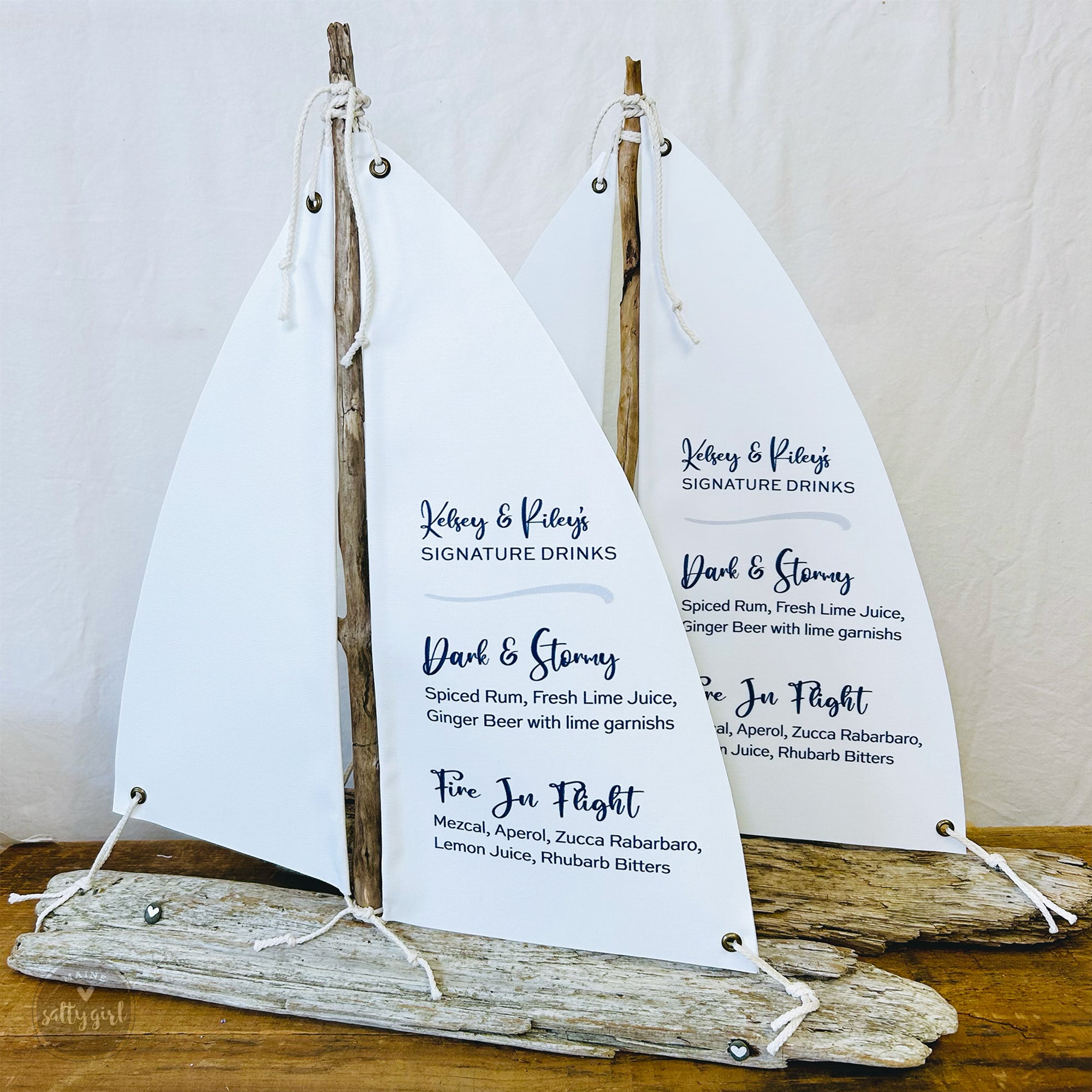 two white sailboat-shaped cocktail menus with black text, displaying a variety of signature drinks.