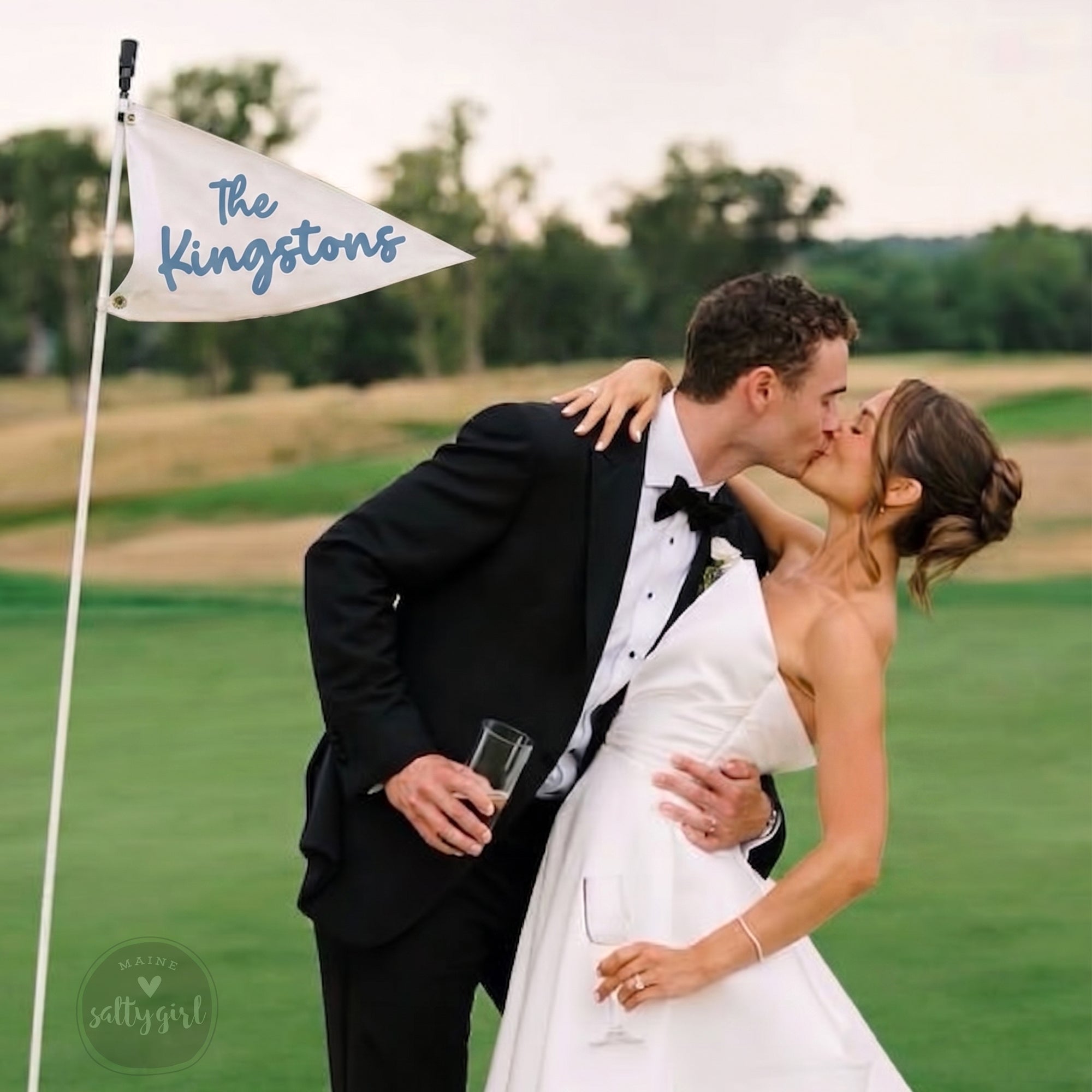 A newly married couple embracing and kissing on a golf course, with a "The Kings" flag in the background.
