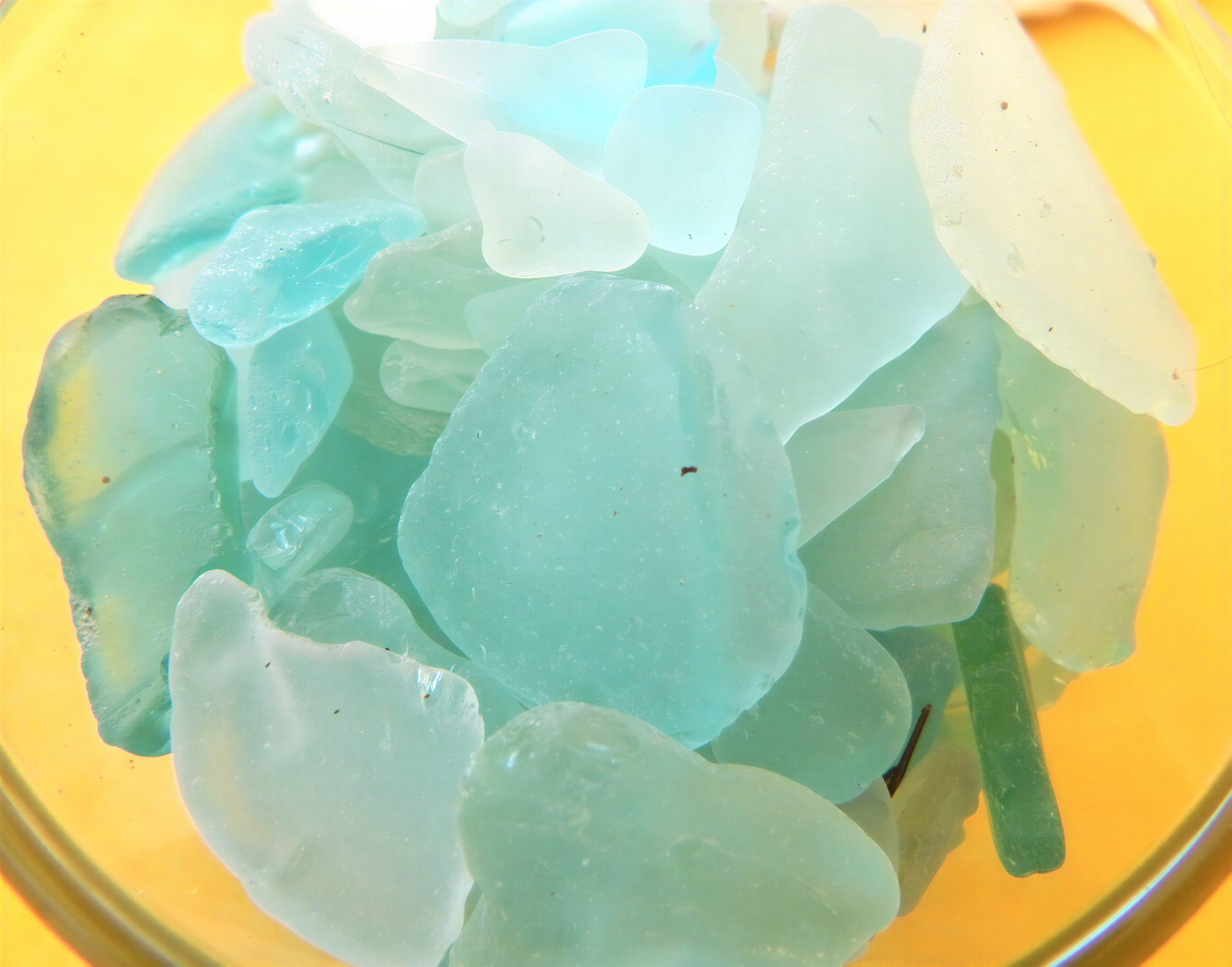 A close-up image of a pile of various shades of blue and green sea glass or similar materials, arranged in a bowl or container.