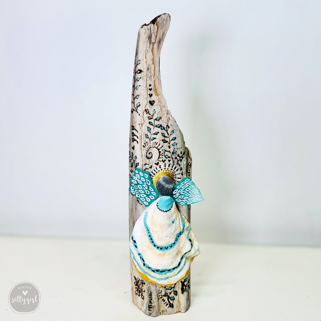 A handcrafted wooden angel figurine with intricate blue and white designs, standing on a white surface.