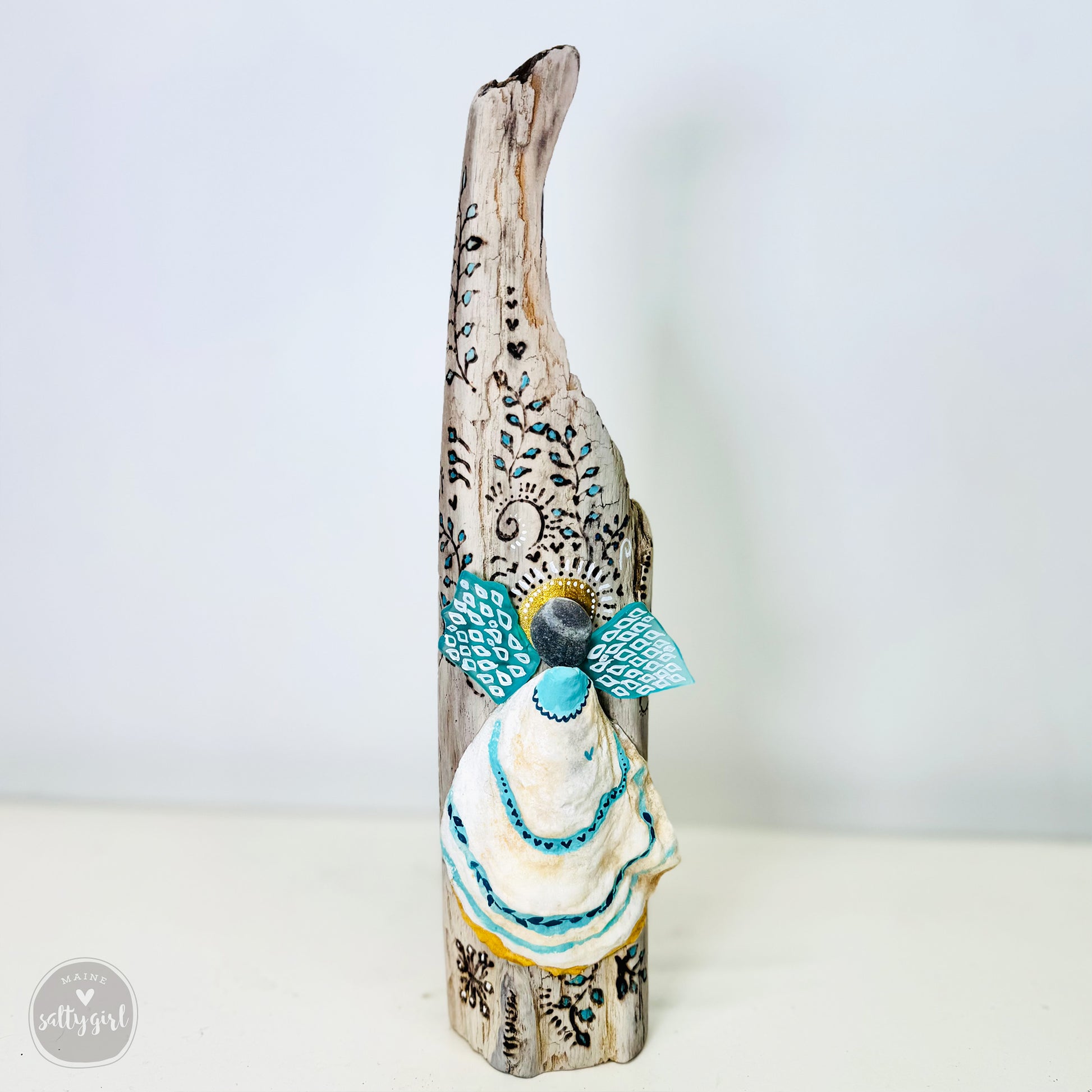 A handcrafted wooden angel figurine with intricate blue and white designs, standing on a white surface.