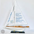 A model sailboat with a white hull and blue sails, displaying a list of signature cocktails on its sails.