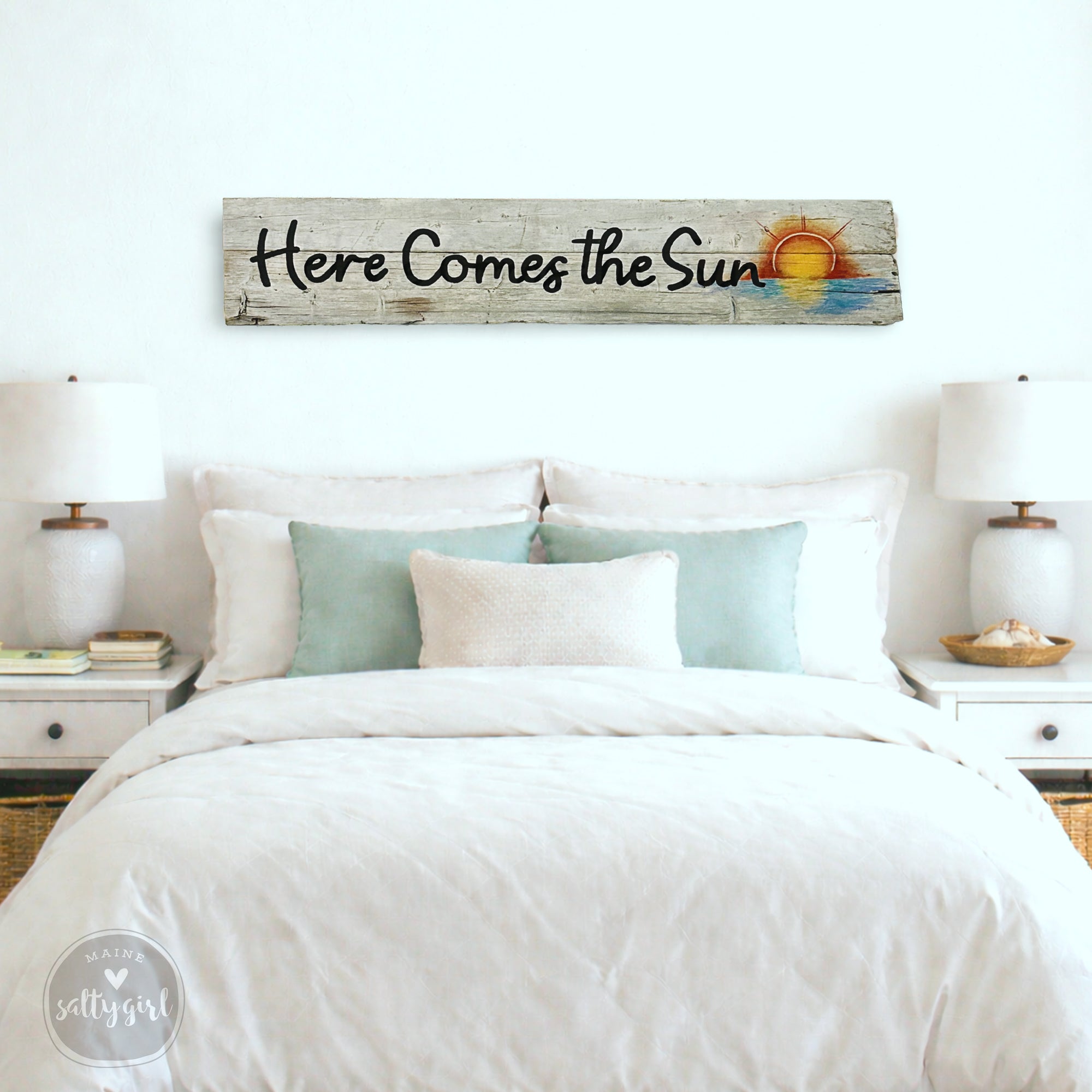 a bedroom with a bed, white bedding, and a wooden sign above it that says "Here Comes the Sun".