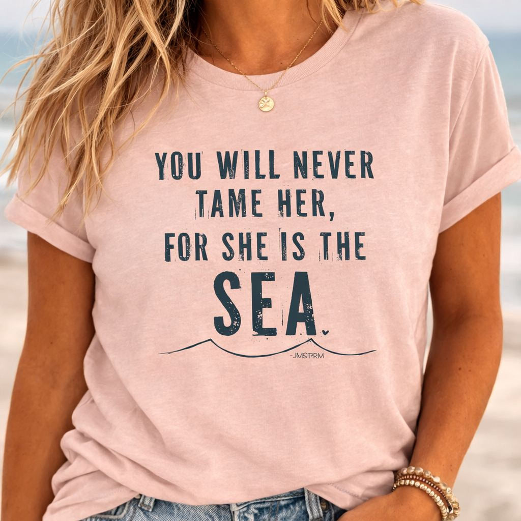 A woman wearing a pink t-shirt with the text "You will never tame her, for she is the sea" printed on it.