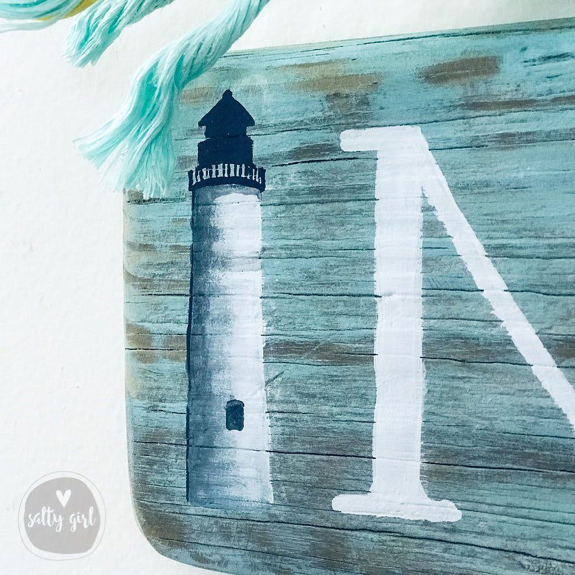 a wooden sign with a lighthouse painted on it, along with a teal rope.