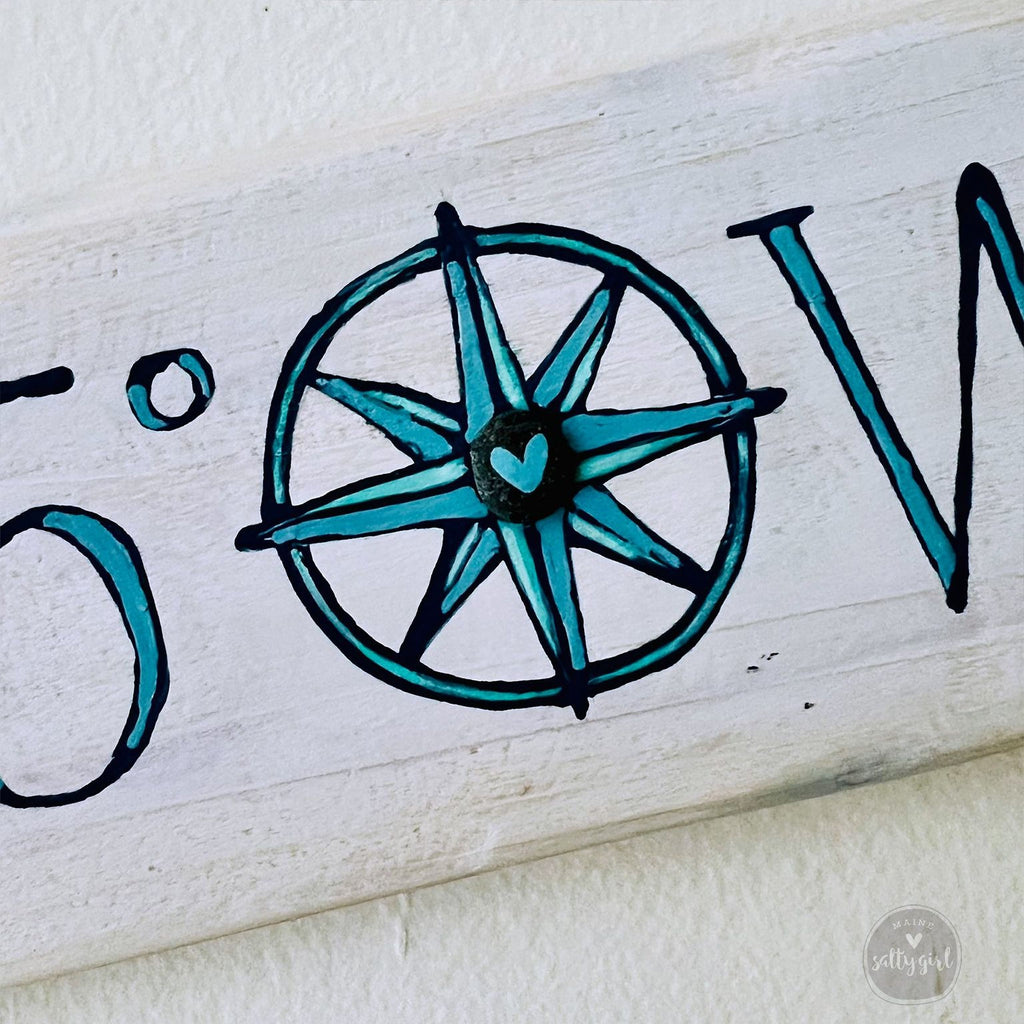 A wooden sign with a compass design and a heart symbol, along with some text.