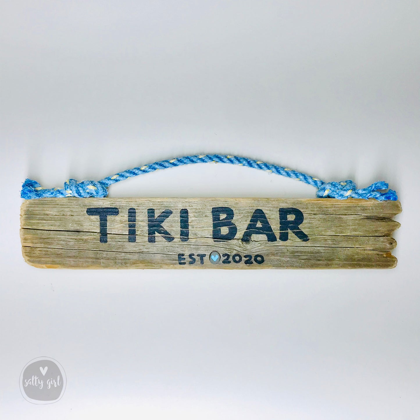 A wooden sign with the text "Tiki Bar" and "EST. 2020" printed on it, along with a blue rope handle.