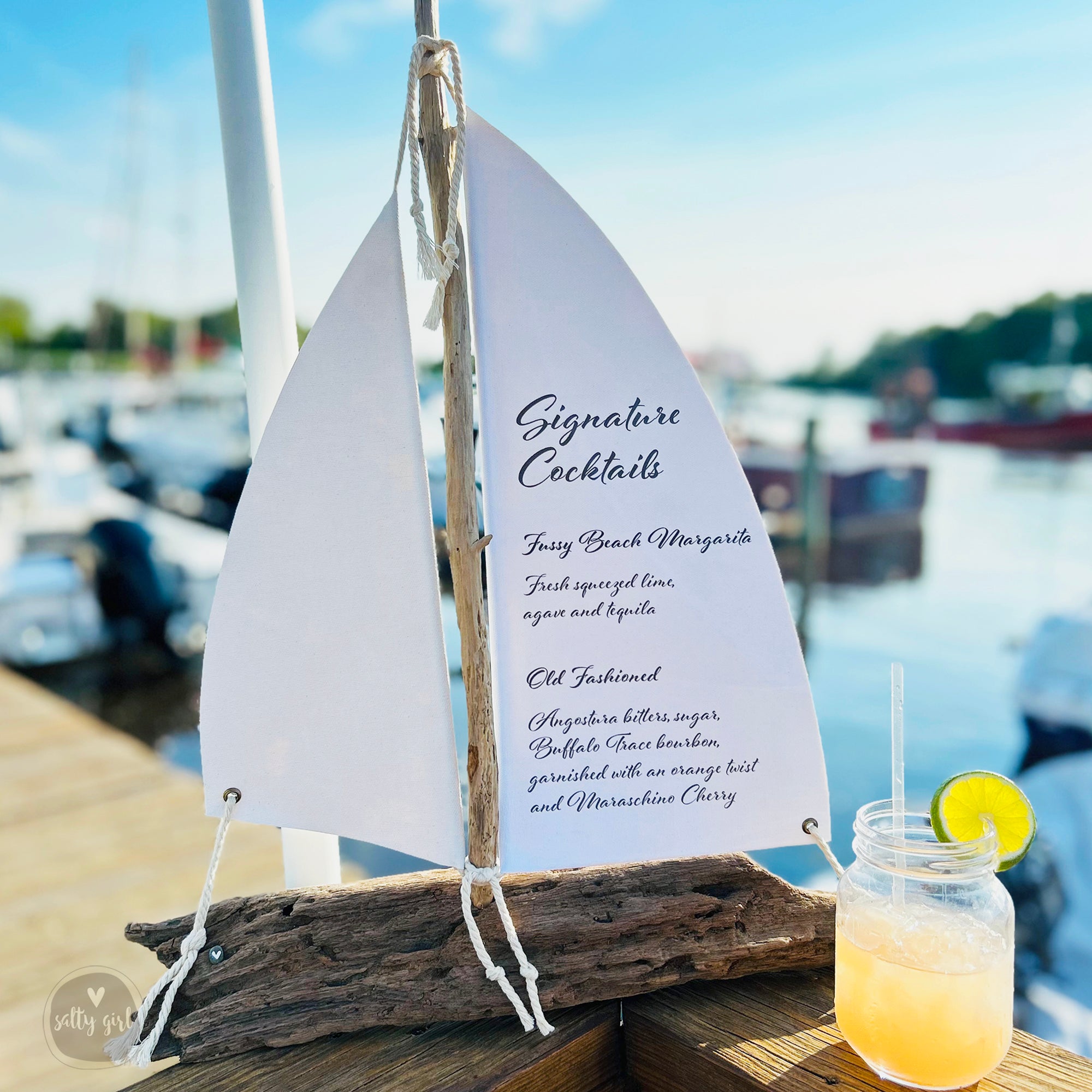 a cocktail menu displayed on a wooden table, with a glass of orange drink and a lemon slice nearby.