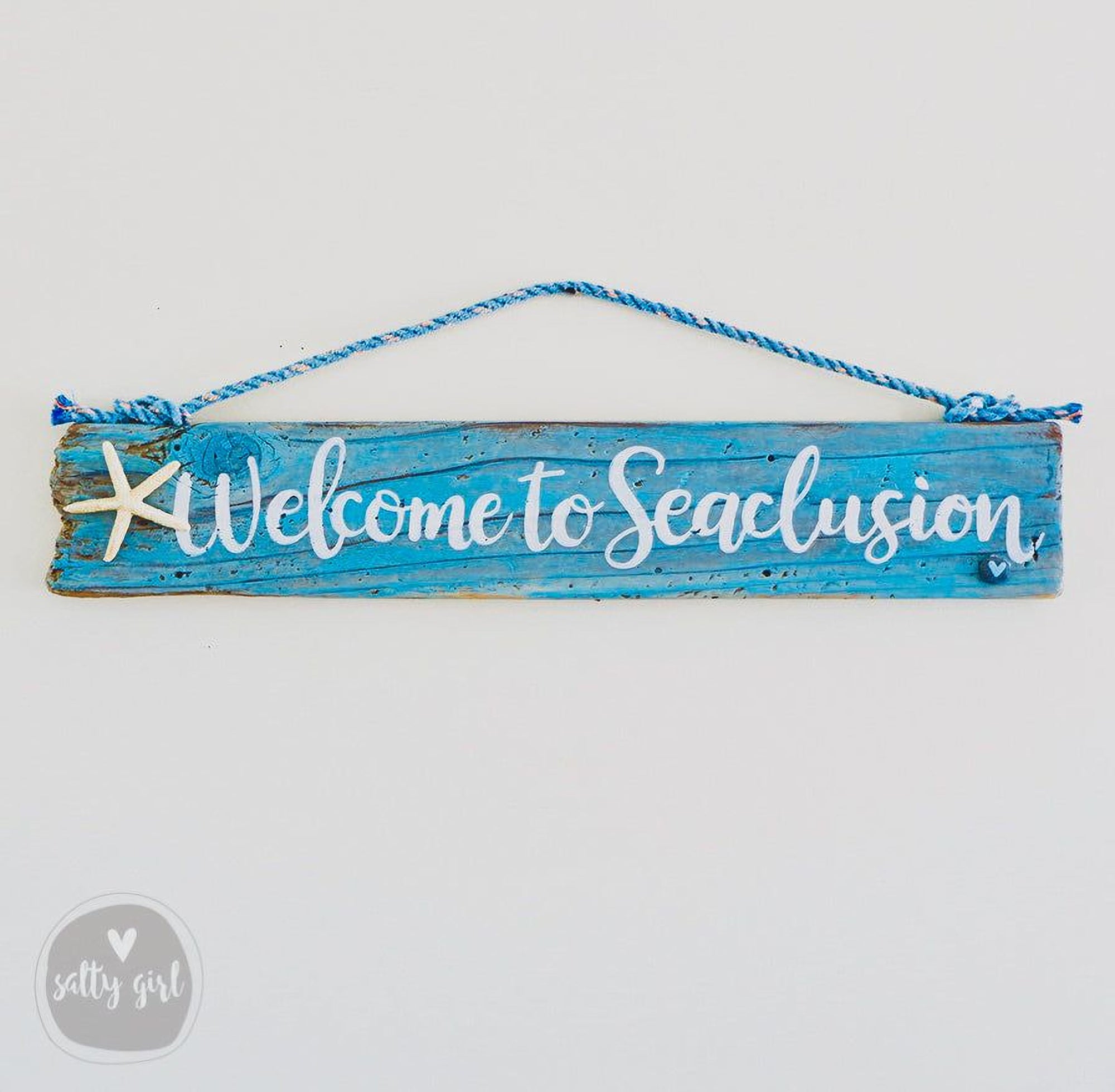 A blue wooden sign with the text "Welcome to Seacclusion" written on it, hanging on a wall.