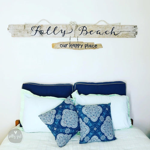a bedroom with a bed adorned with blue and white patterned pillows. Above the bed, there is a wooden sign that reads "Folly Beach our happy place".