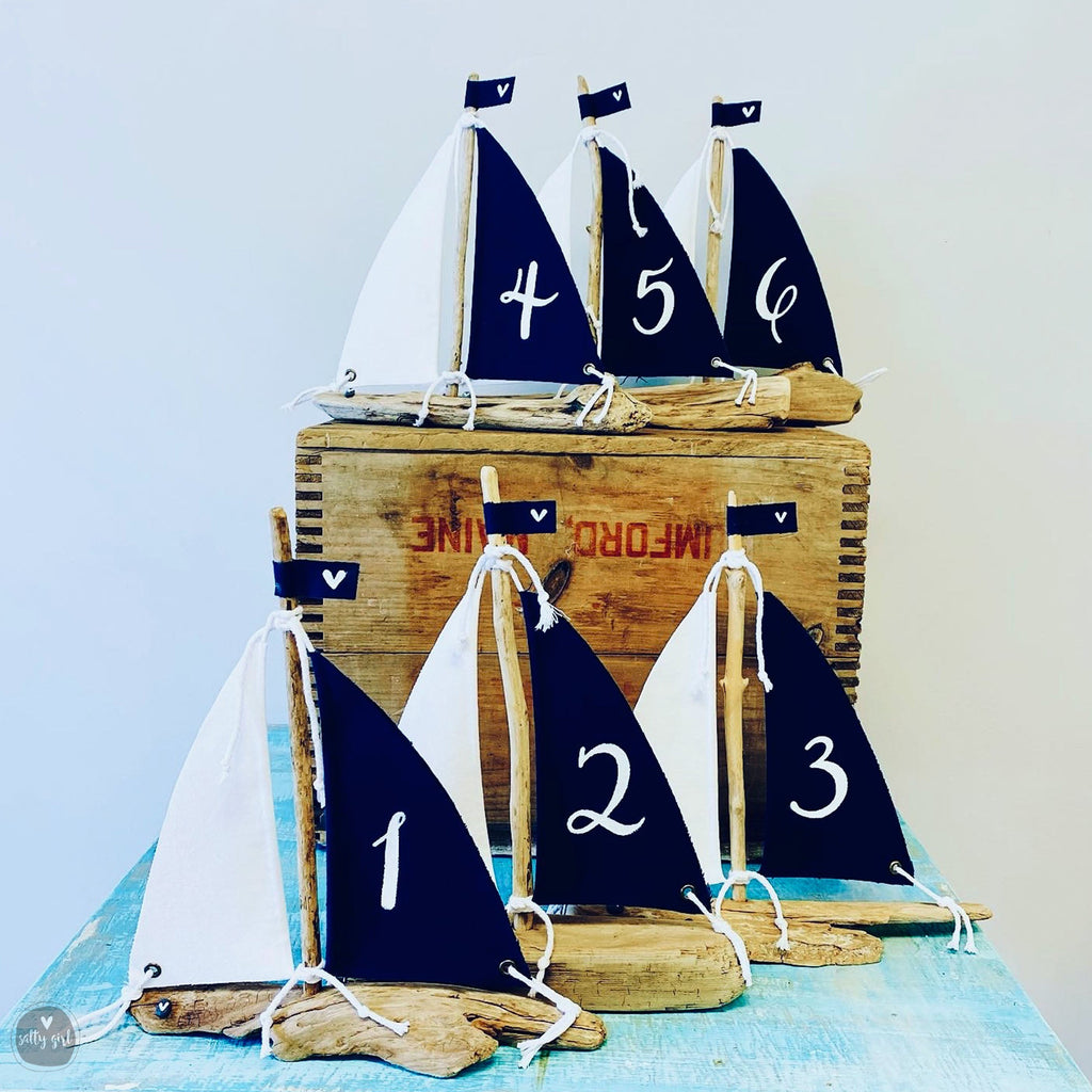 A collection of six blue and white sailboat-shaped decorations, each with a number on it, displayed on a wooden crate.