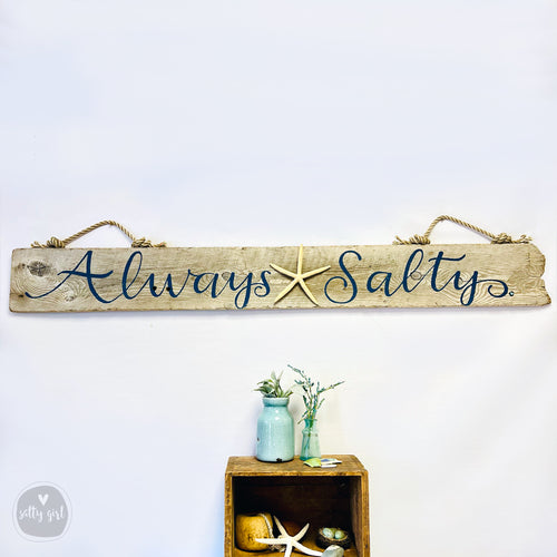 Personalized driftwood wall art hanging in a bright coastal living room, showcasing natural sun-bleached wood textures.