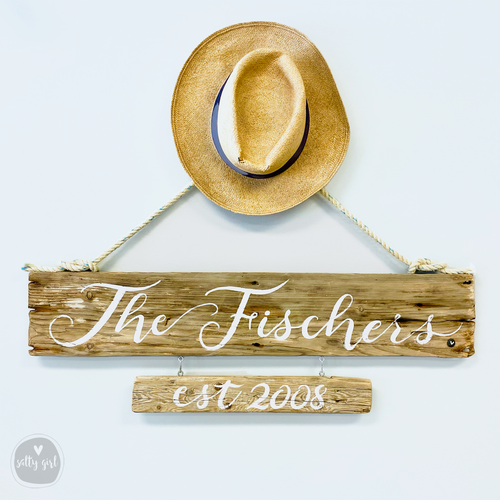 a wooden sign with the name "The Fischers" and the year "est 2008" written on it, hanging on a wall. Above the sign, there is a straw hat hanging on a rope.