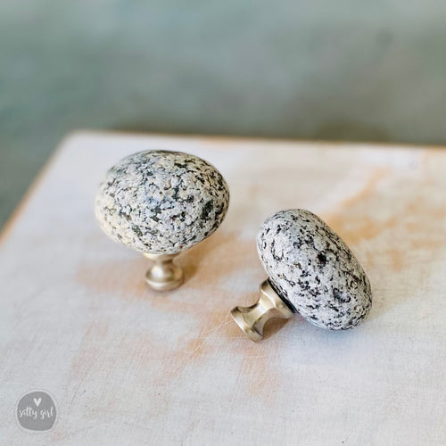 two stone knobs or handles, one standing upright and the other lying on its side, both placed on a wooden surface.