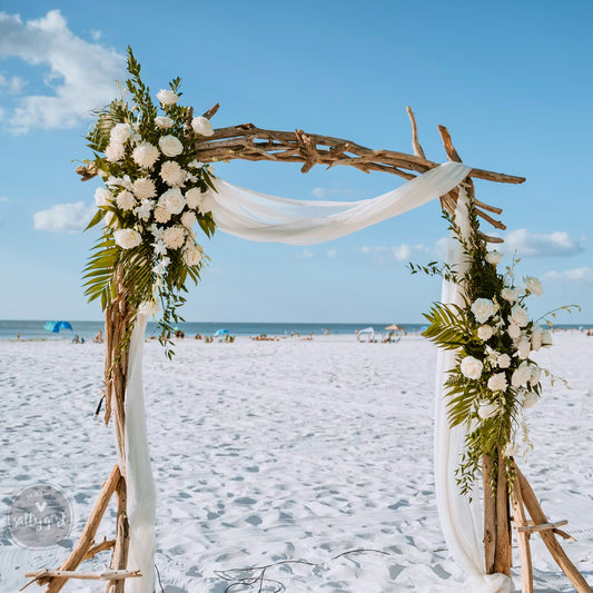 a wooden arch decorated with flowers and greenery on a beach