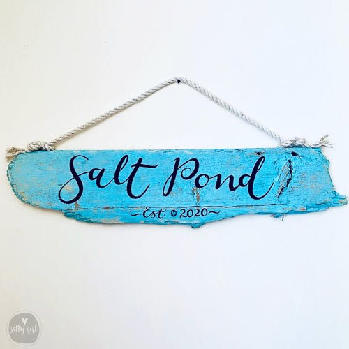 A blue wooden sign with the text "Salt Pond est 2020" hanging on a rope.