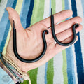 A hand holding two black metal hooks against a striped background.